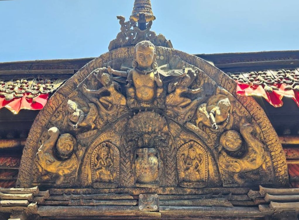 Sculpted arch at Guhyeshwari Temple with a central figure, surrounding reliefs and red cloth along the roof edge.