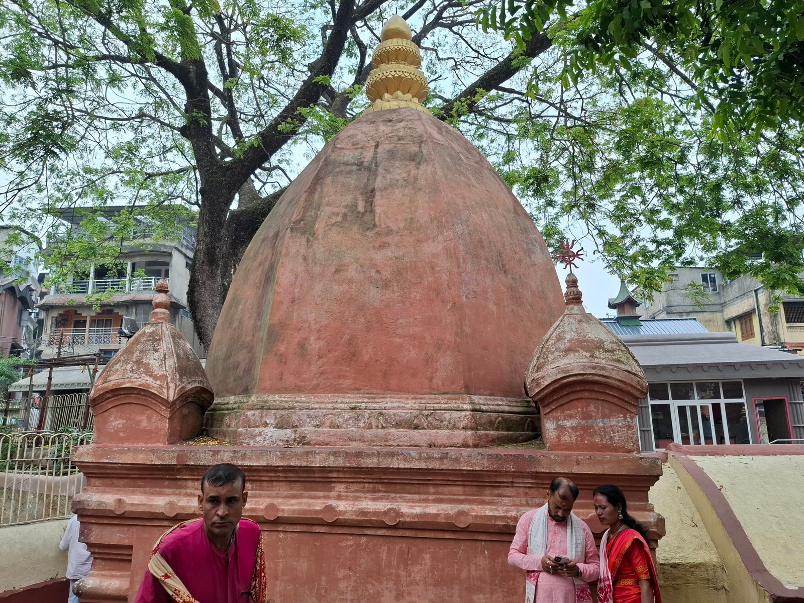 Red domed shrine of Kamakhya Temple above a crowded courtyard, surrounded by trees.
