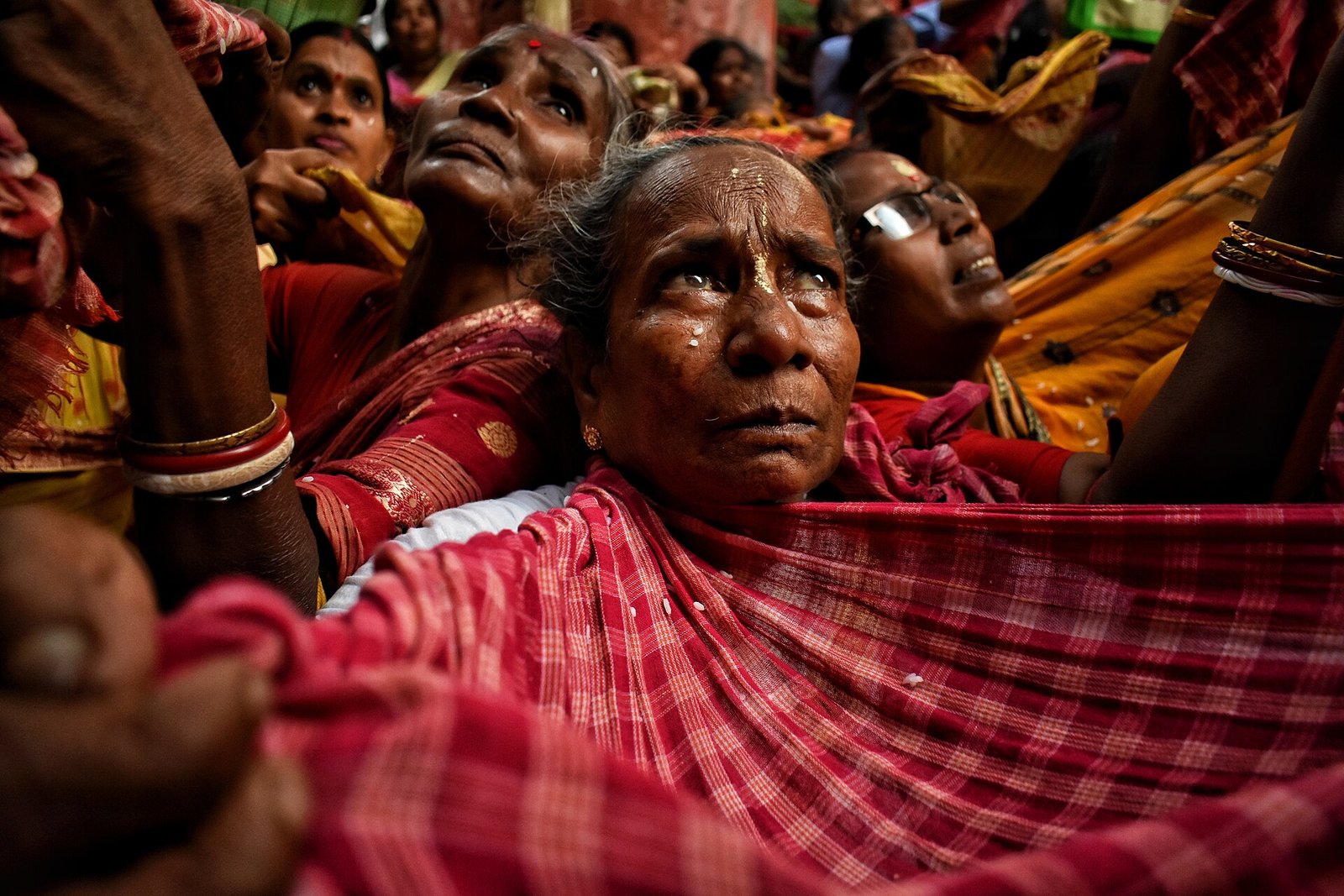 Worshippers hold out sari cloths to receive rice prasad, with grains visible on the cloth in the foreground.