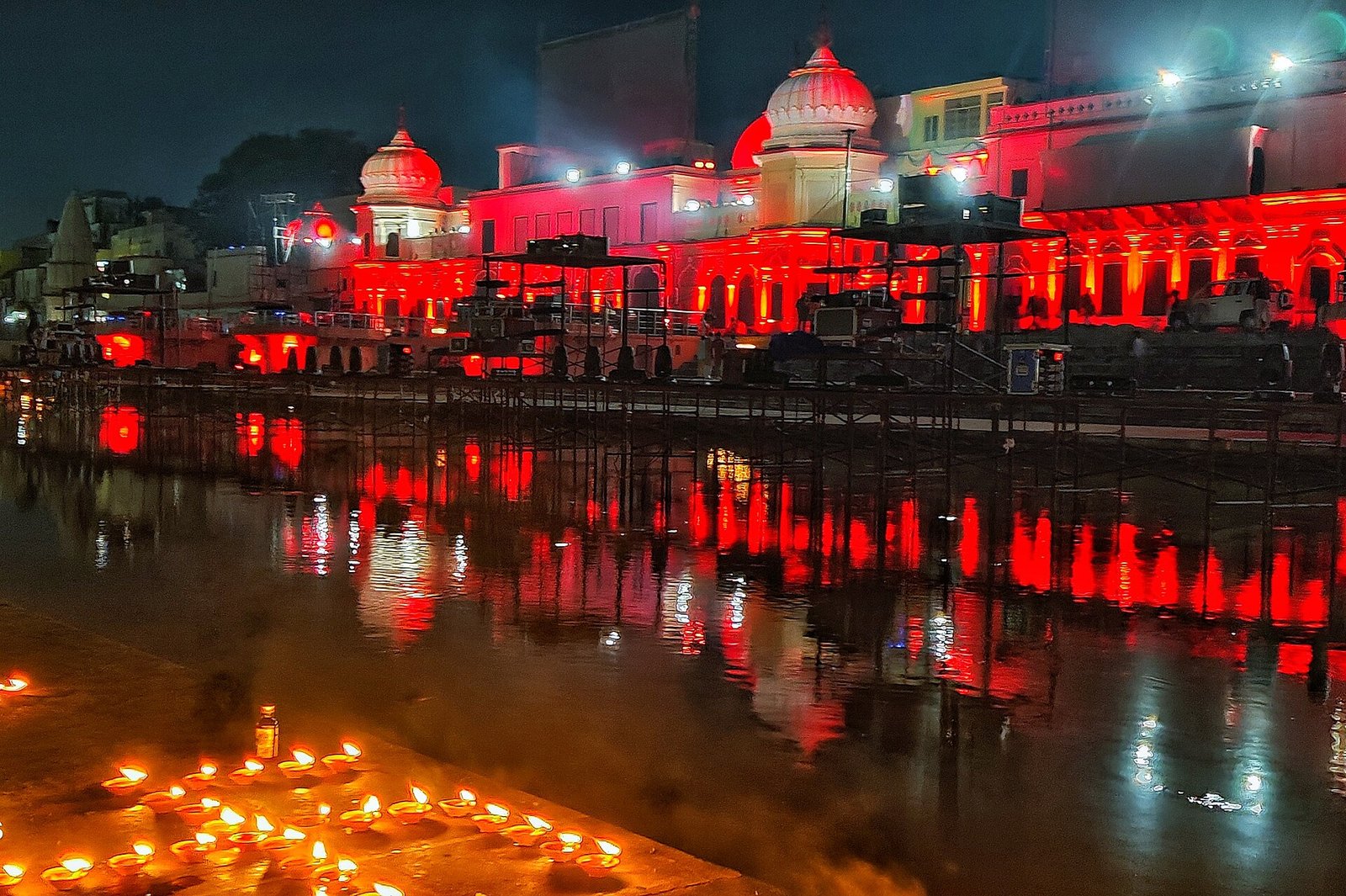 Earthen lamps burn beside water reflecting the red-lit facades and domed pavilions of Ayodhya.