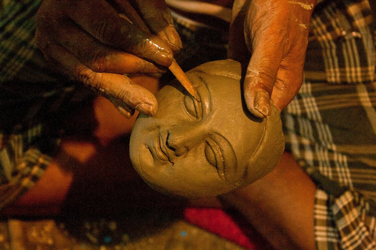 A craftsperson in Kumartuli holds a clay face and uses a pointed tool to shape the eye before Durga Puja.