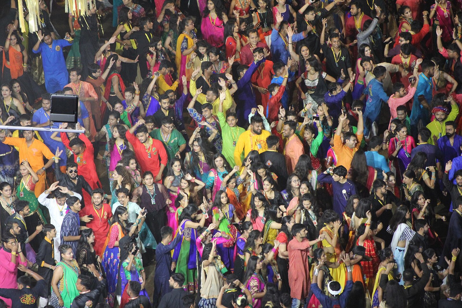 A large group of Garba dancers in colorful kurtas, skirts and saris raise their arms during a nighttime celebration in Vadodara, Gujarat.