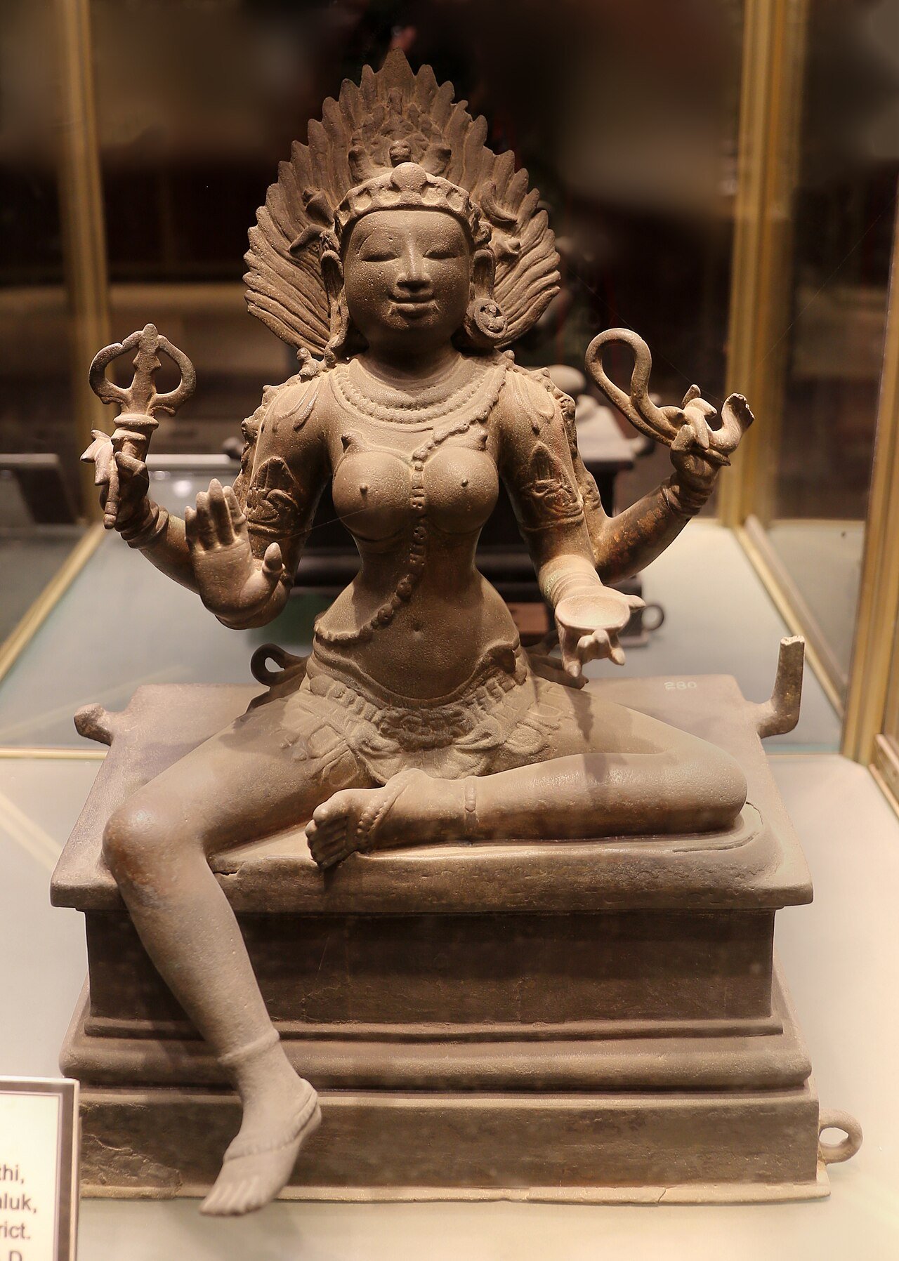Seated four-armed Chola bronze of Kali with flame-like hair, a trident, a looped snake and a cup.