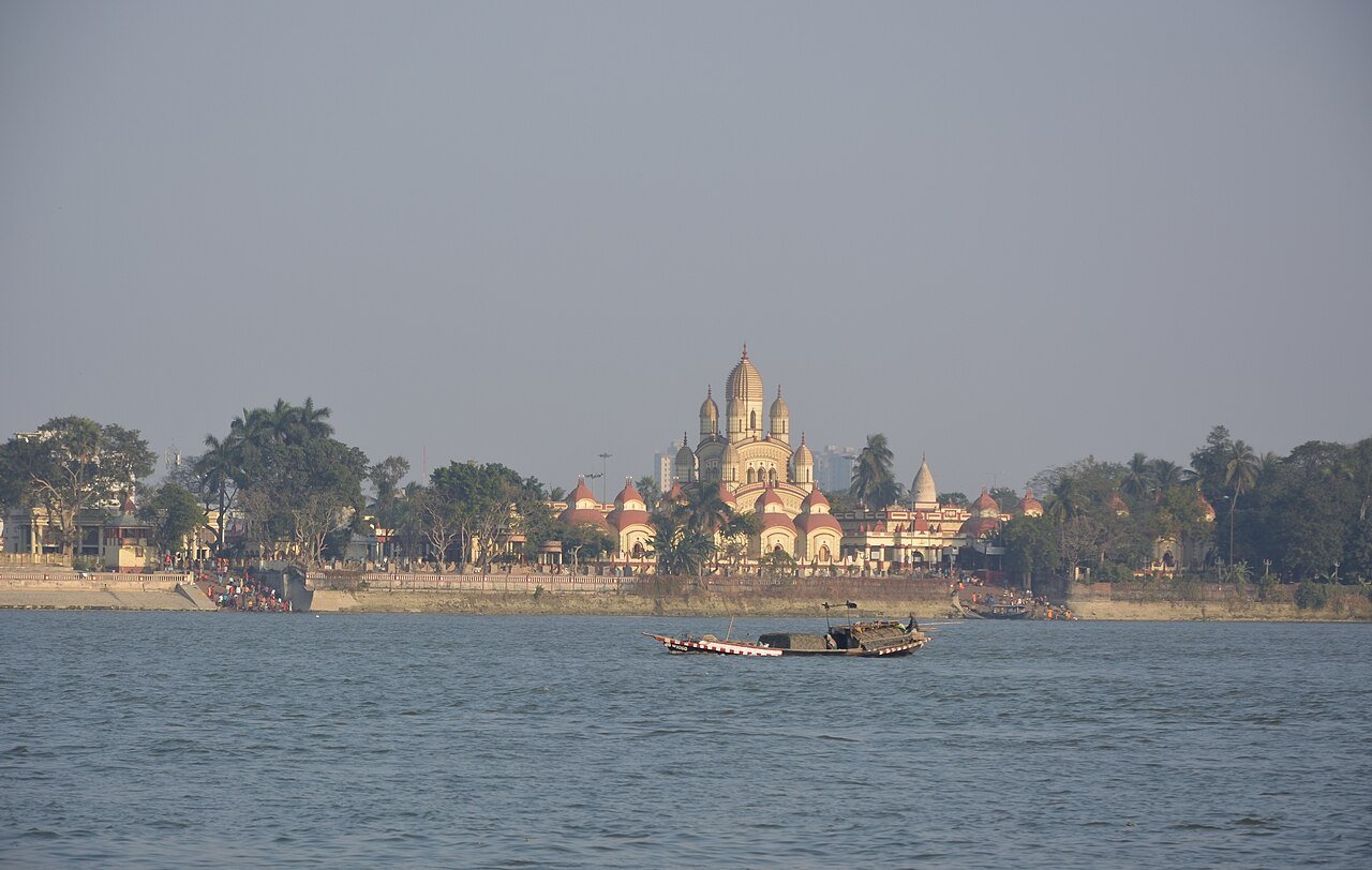 Dakshineswar Kali Temple and riverside buildings seen across the Hooghly River, with boats in the foreground.