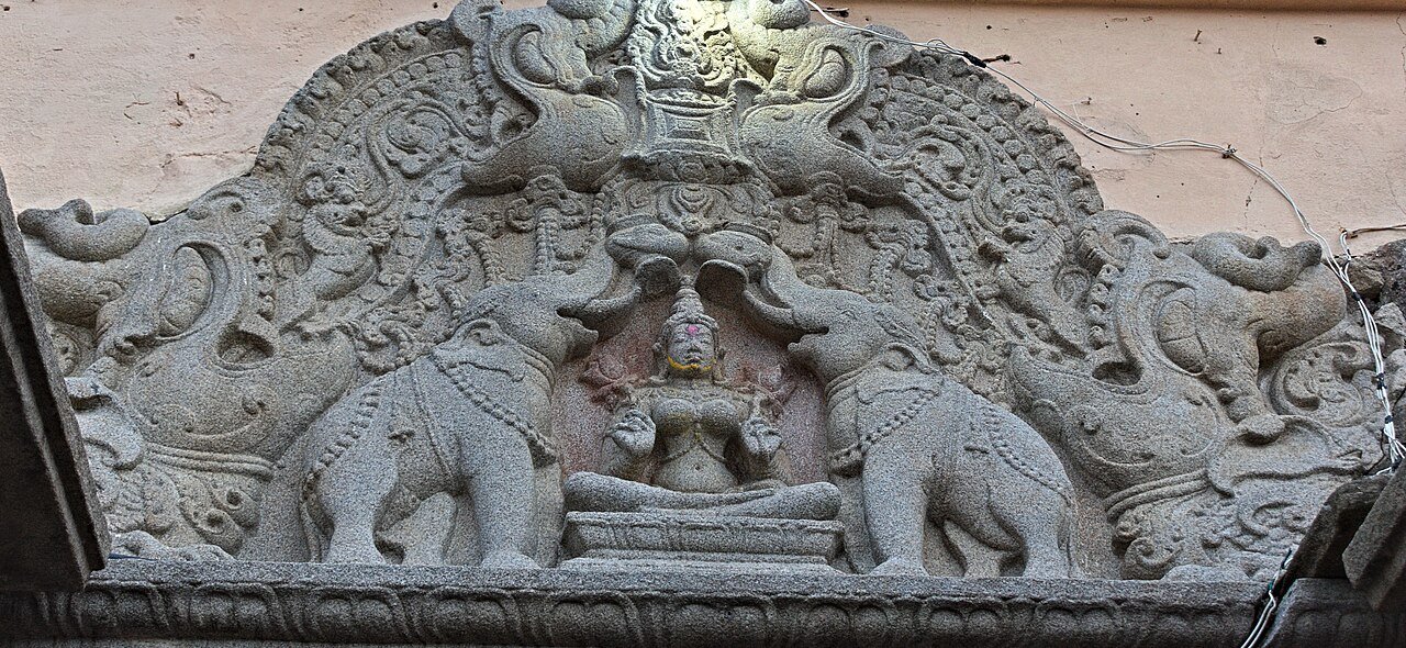 Stone doorway relief of seated Gajalakshmi flanked by two elephants raising vessels above her, beneath a carved arch.