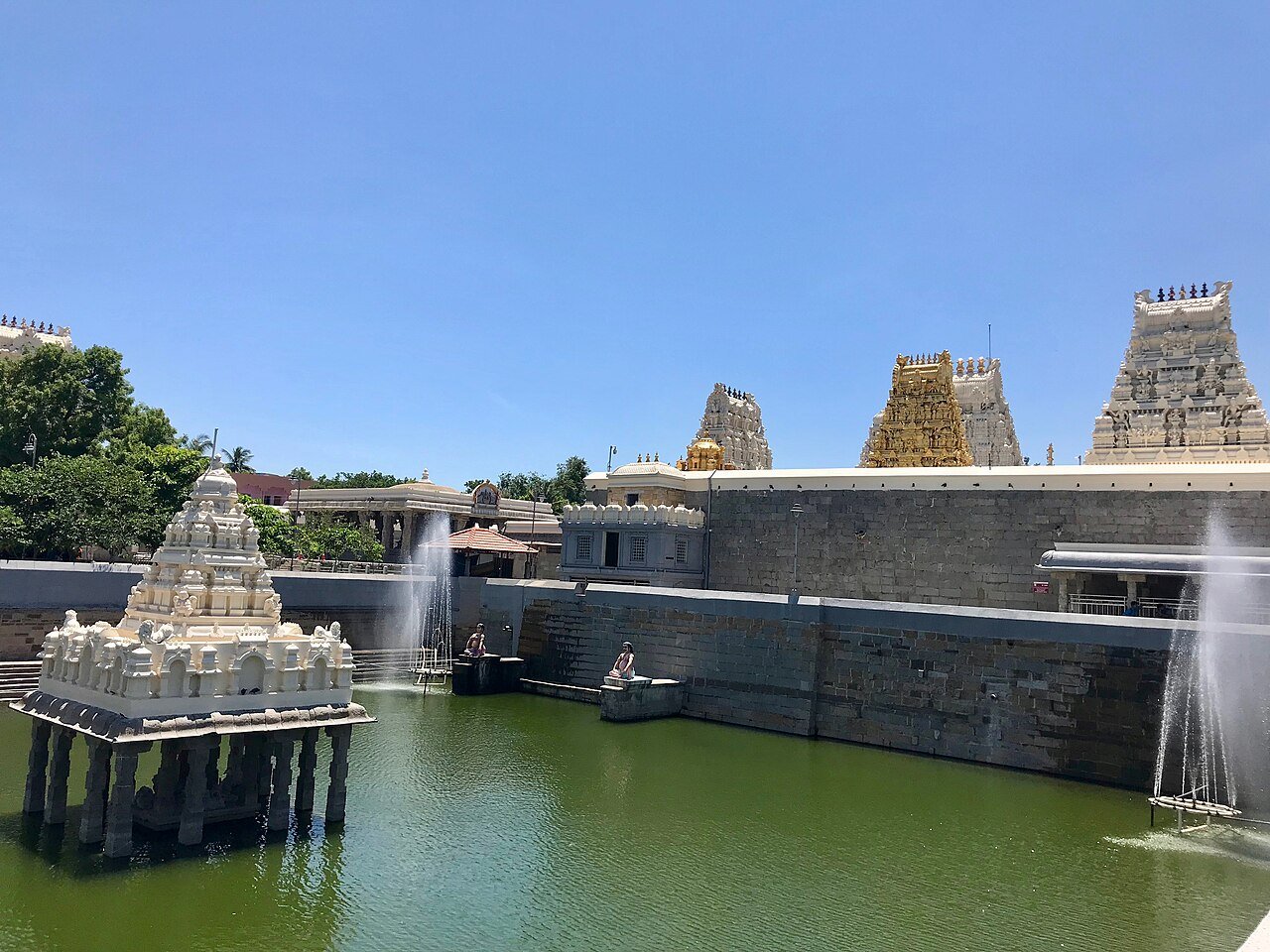 Kamakshi Amman Temple in Kanchipuram, with white and gold towers rising beyond a green temple tank and a pavilion standing in the water.